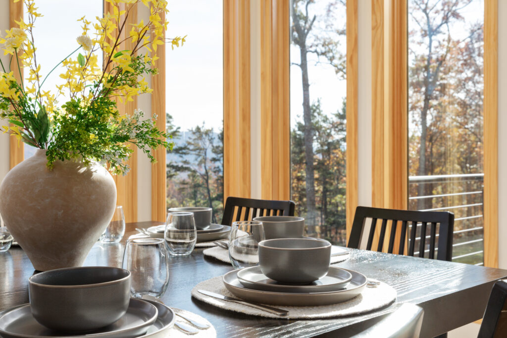 Dining table set beside floor-to-ceiling windows with forest and mountain views at The Vale in Lost River, West Virginia