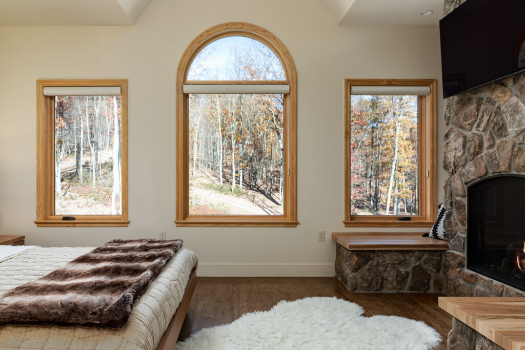 The Vale primary bedroom with stone fireplace, ensuite bathroom, arched windows and forest views, Lost River West Virginia