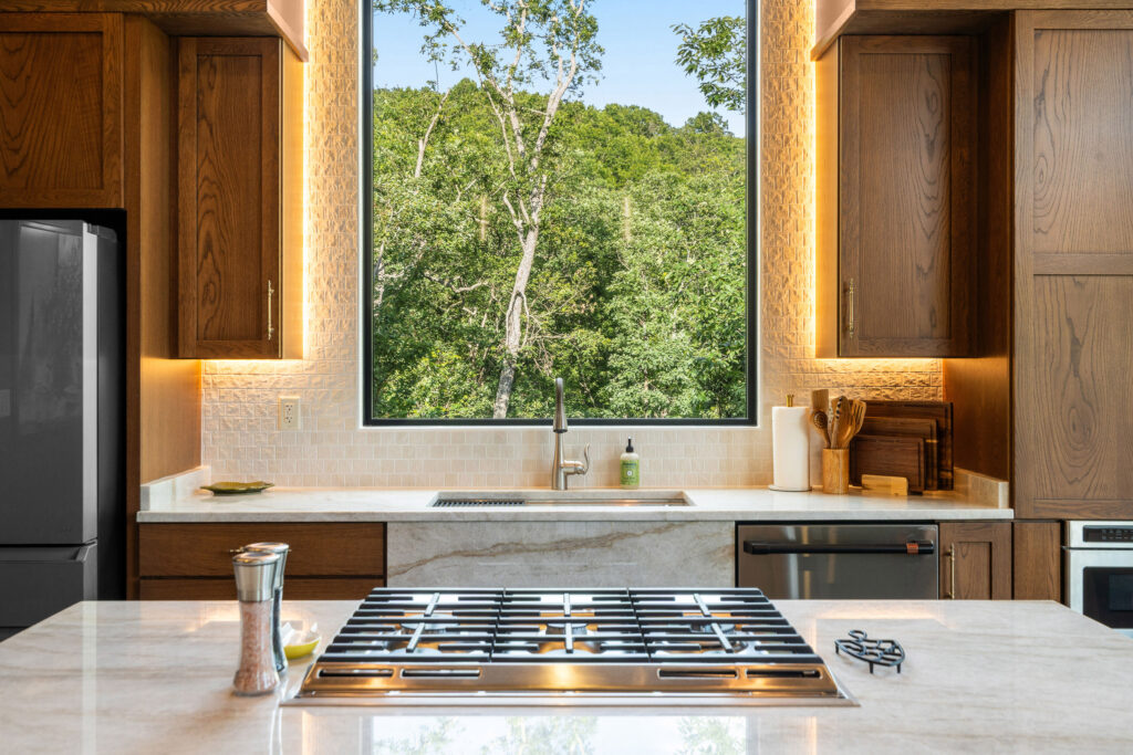 Kitchen island with gas cooktop and forest-view window at The Nook
