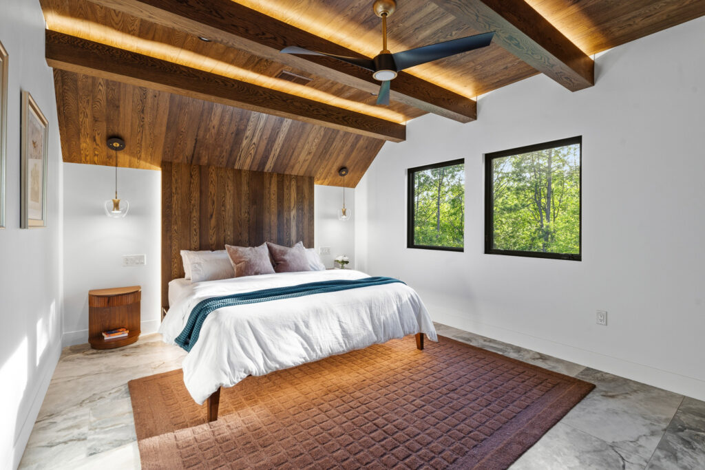 Guest bedroom with wood-plank ceiling, ceiling fan, and patterned rug at The Nook