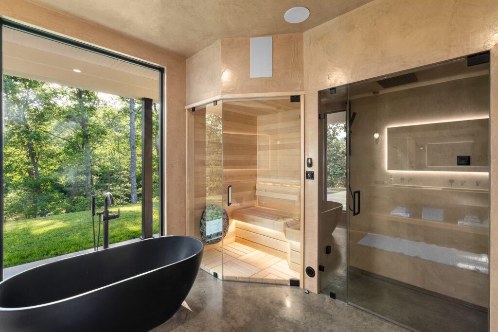 Black freestanding soaking tub beside a large window, with a dry sauna & steam shower at The Nook luxury cabin