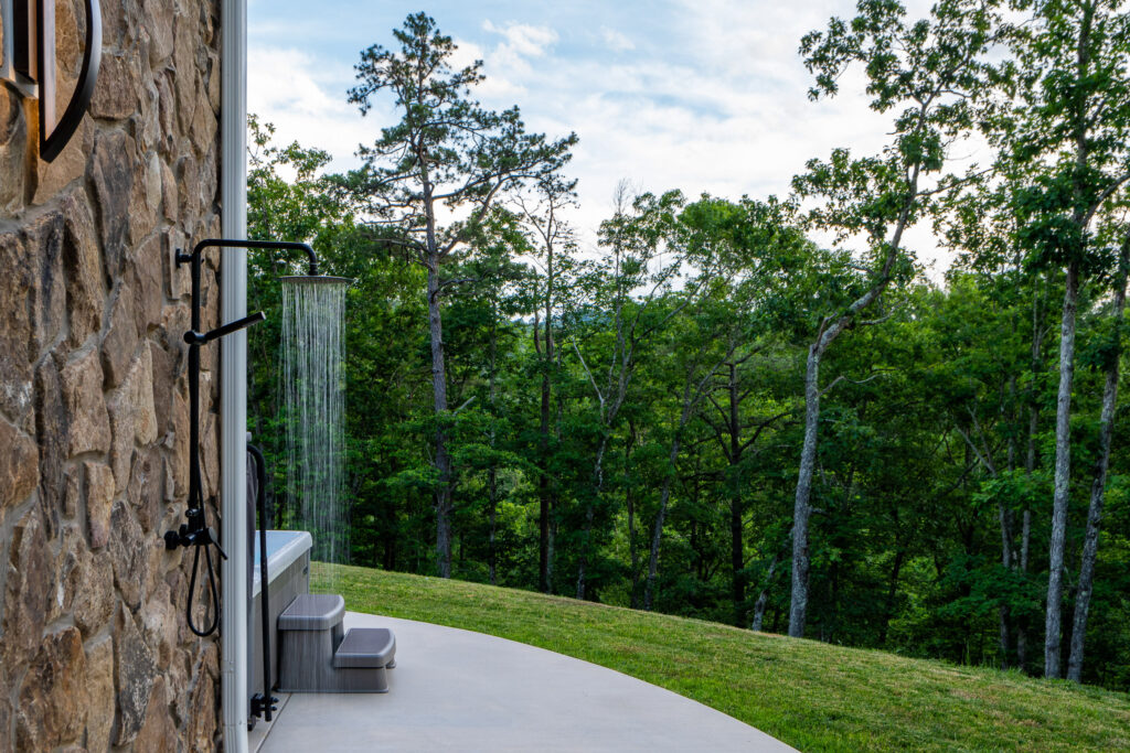 View of the green lawn, outdoor shower and surrounding forest at The Nook in Lost River, WV